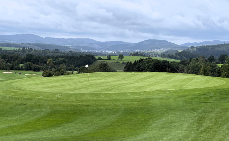 Ein Green auf einem Golfplatz, im Hintergrund eine Stadt