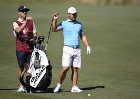 Tom Kim nimmt einen Schläger aus seinem Golfbag. Daneben steht sein Caddie