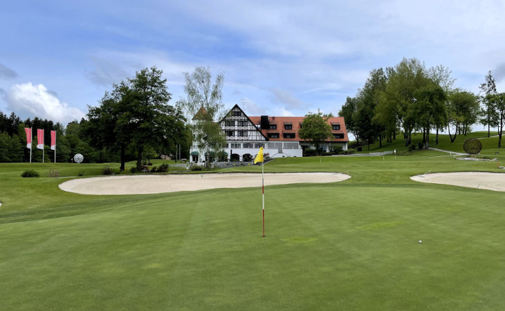 Ein Green auf einem Golfplatz, im Hintergrund das Clubhaus