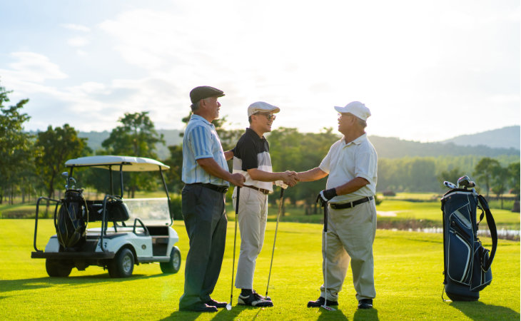 Asiatische Geschäftsleute schütteln sich auf dem Golfplatz die Hände