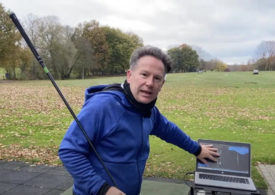Golflehrer Paul Dyer hält einen Schläger und zeigt auf einen Laptop