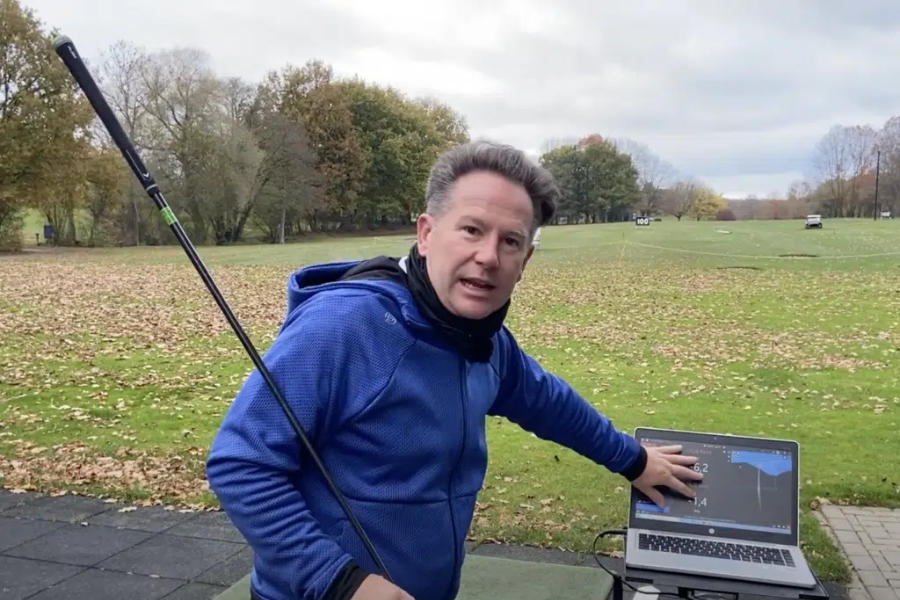 Golflehrer Paul Dyer hält einen Schläger und zeigt auf einen Laptop