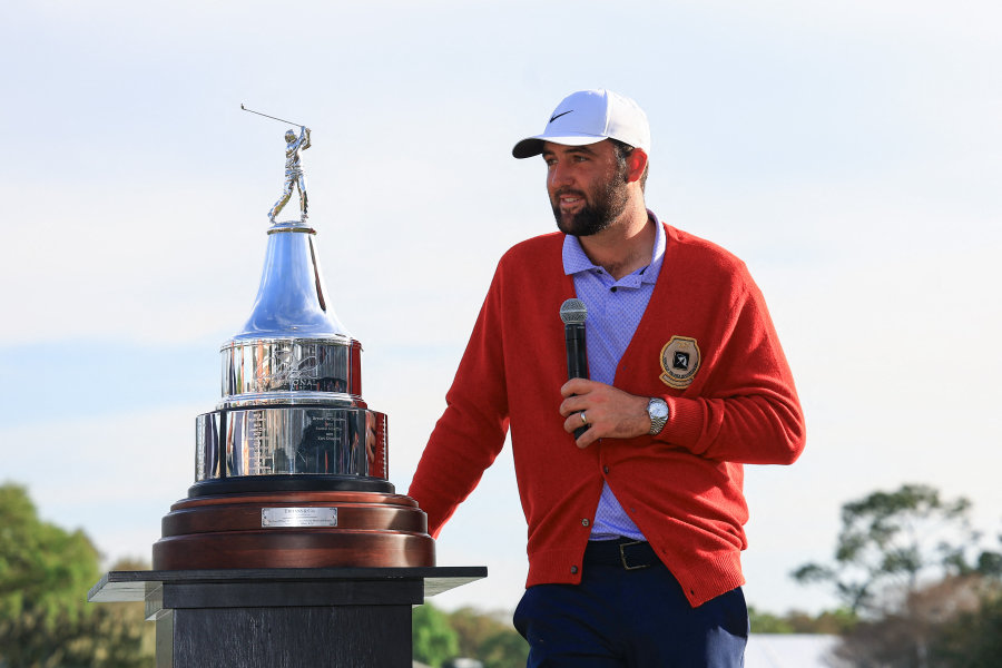 Scottie Scheffler in der roten Jacke des Arnold Palmer Invitational spricht mit einem Mikrofon in der Hand vor der Trophäe