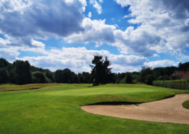 Ein Sandbunker, Bäume und ein Hausdach auf einem Golfplatz
