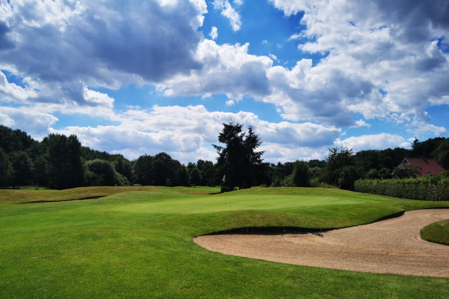 Ein Sandbunker, Bäume und ein Hausdach auf einem Golfplatz